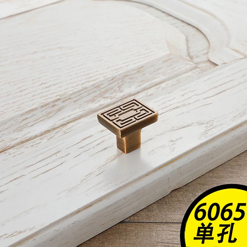 Square bronze vintage cabinet handle with geometric design on white wooden cabinet door