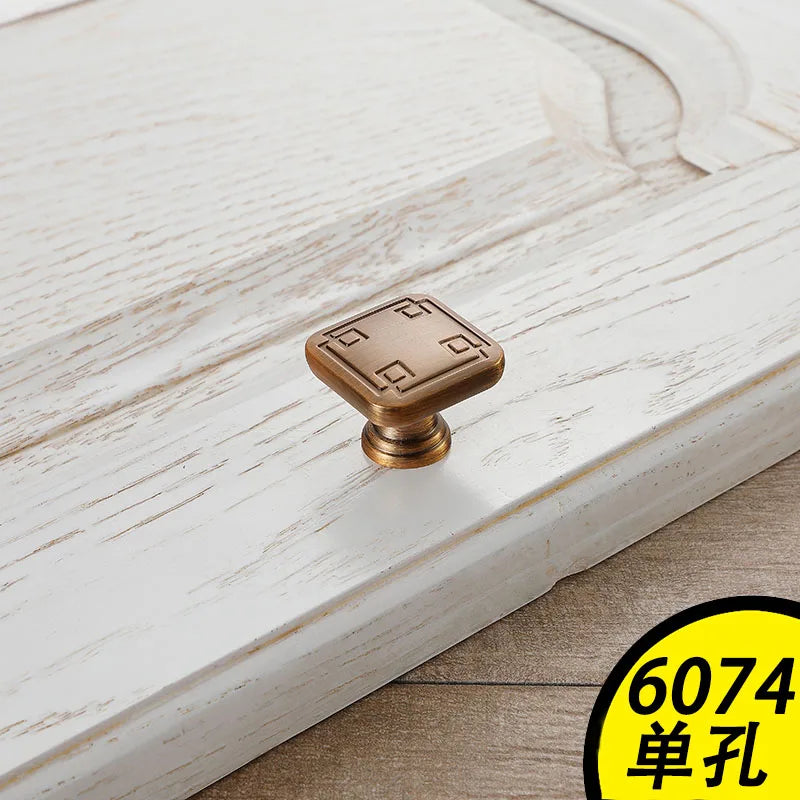 Square bronze Vintage Cabinet Handles with decorative designs installed on distressed white wooden cabinet door