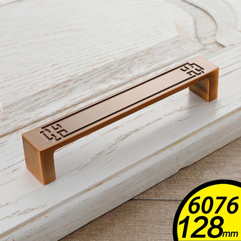 Bronze metal vintage cabinet handles with decorative corner patterns on white wooden drawer