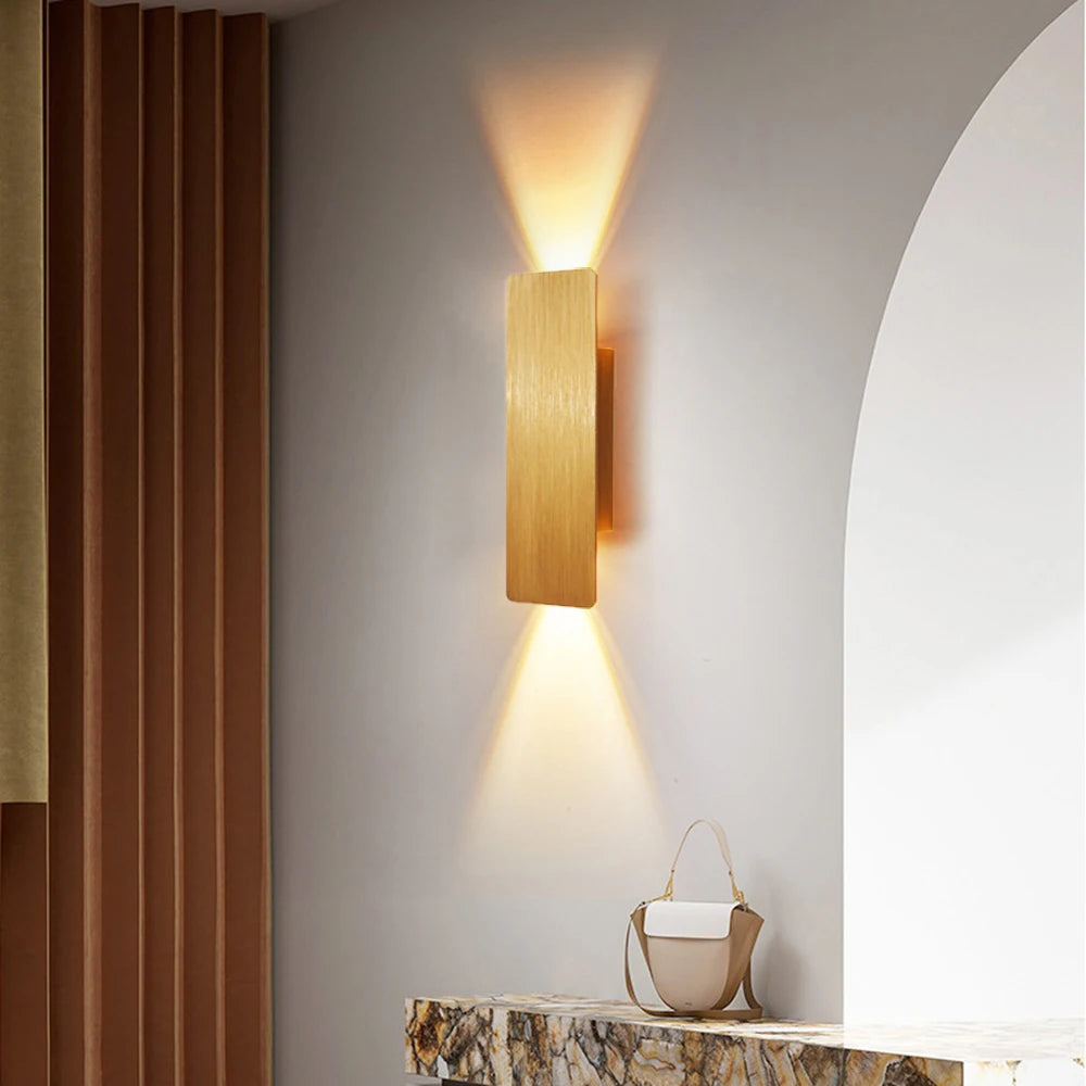 Modern gold LED wall lamp with bi-directional lighting on a textured wall above a marble countertop.