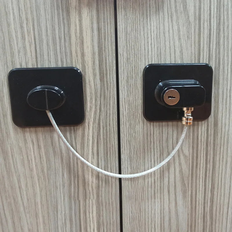 Child safety lock with black base plates and metal cable on wooden cabinet for home security.