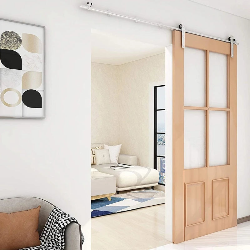 CCJH stainless steel sliding barn door track kit with wooden door and glass panels in a modern living room.