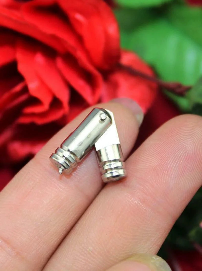Close-up of a pair of copper barrel hinges held between fingers, with a red and green floral background.