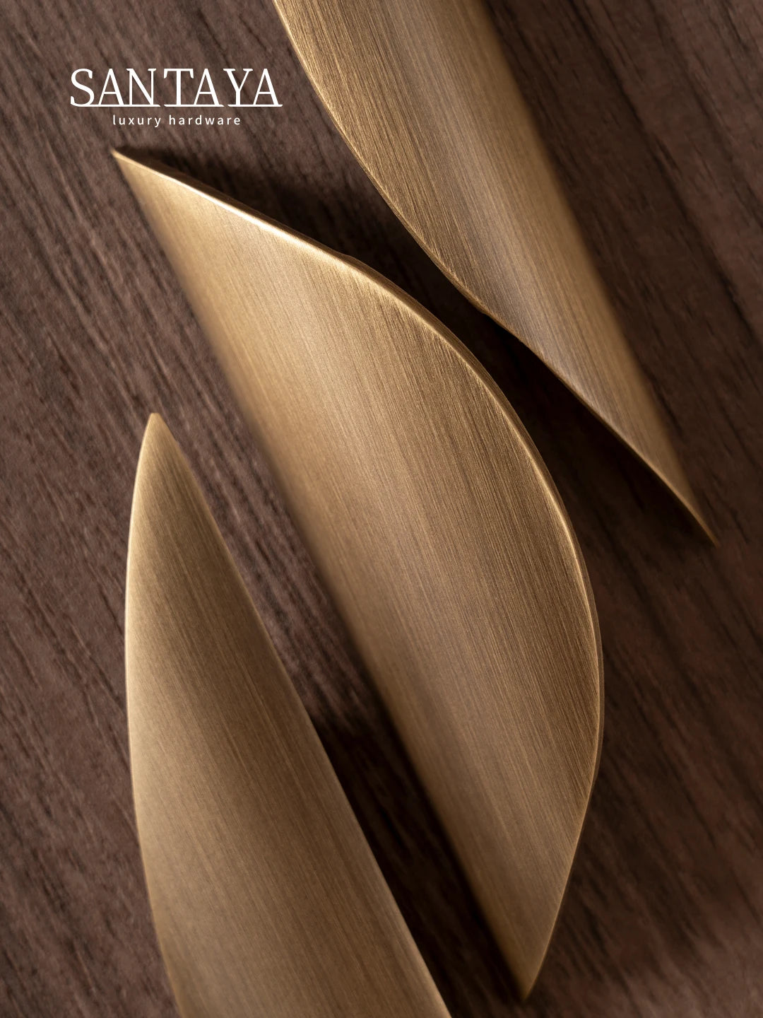 Close-up of three antique brass pulls on a wooden surface, showcasing their elegant curved design and smooth finish.