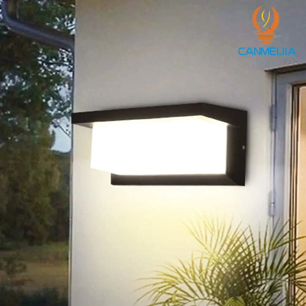 LED wall lamp with black frame and frosted diffuser, mounted on an exterior wall with greenery in the background.