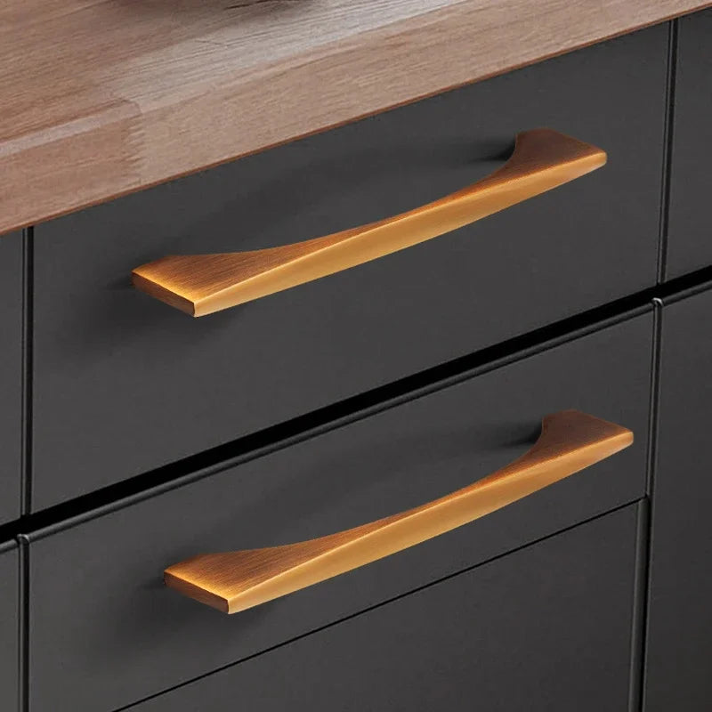 Classical antique cabinet handles in brass with a yellow bronze finish on a modern dark drawer.