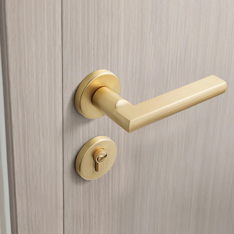 Golden luxury indoor bedroom door lock with a matte brushed finish on a light wooden door, showcasing a modern rectangular handle and silent operation.