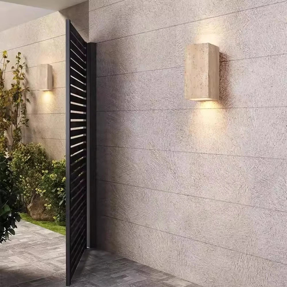 Outdoor waterproof travertine wall light in a courtyard setting with stone walls and greenery.