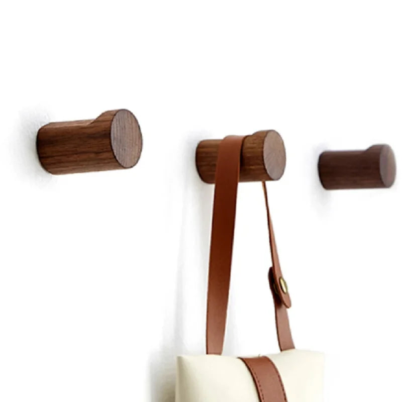 Modern minimalist walnut coat hooks mounted on a white wall, holding a bag strap.