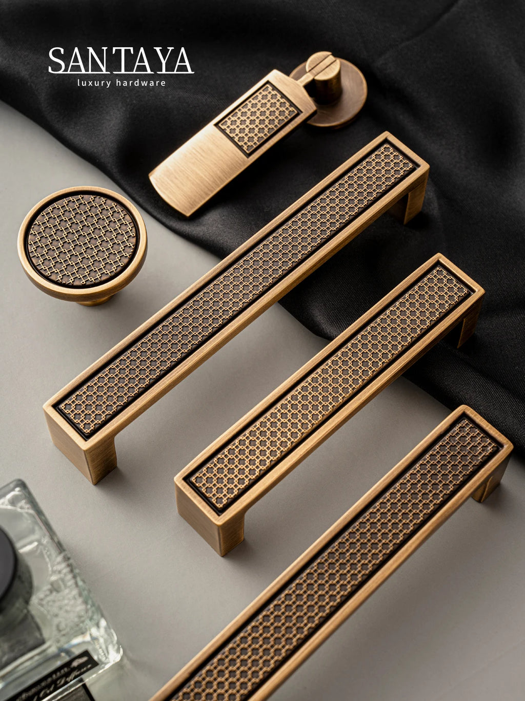 Antique brass handle and knob set with luxury bronze finish and geometric pattern, displayed on fabric.