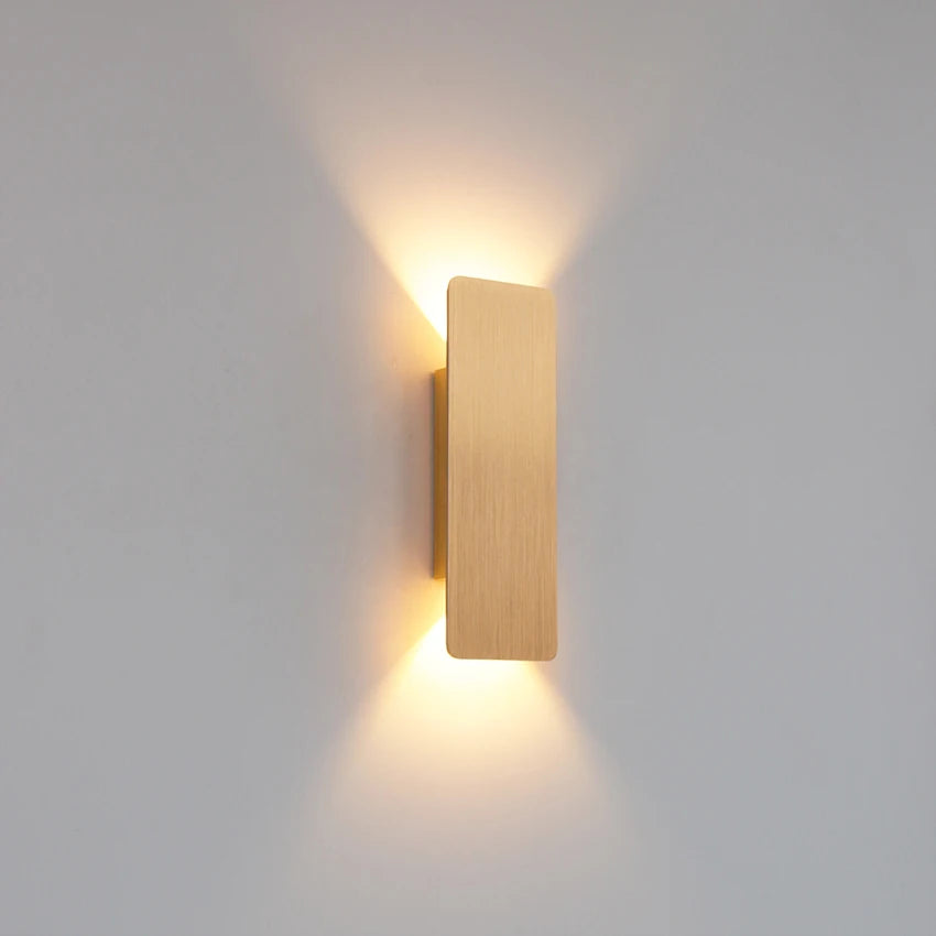 Modern LED wall lamp with a rectangular metallic design and warm light glow, mounted on a light-colored wall.