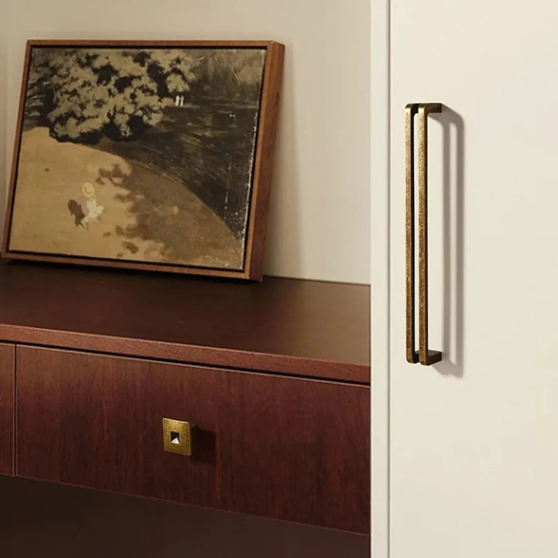 Premium Nordic style gold furniture handle on a light-colored cabinet with a wooden surface and framed artwork in the background.