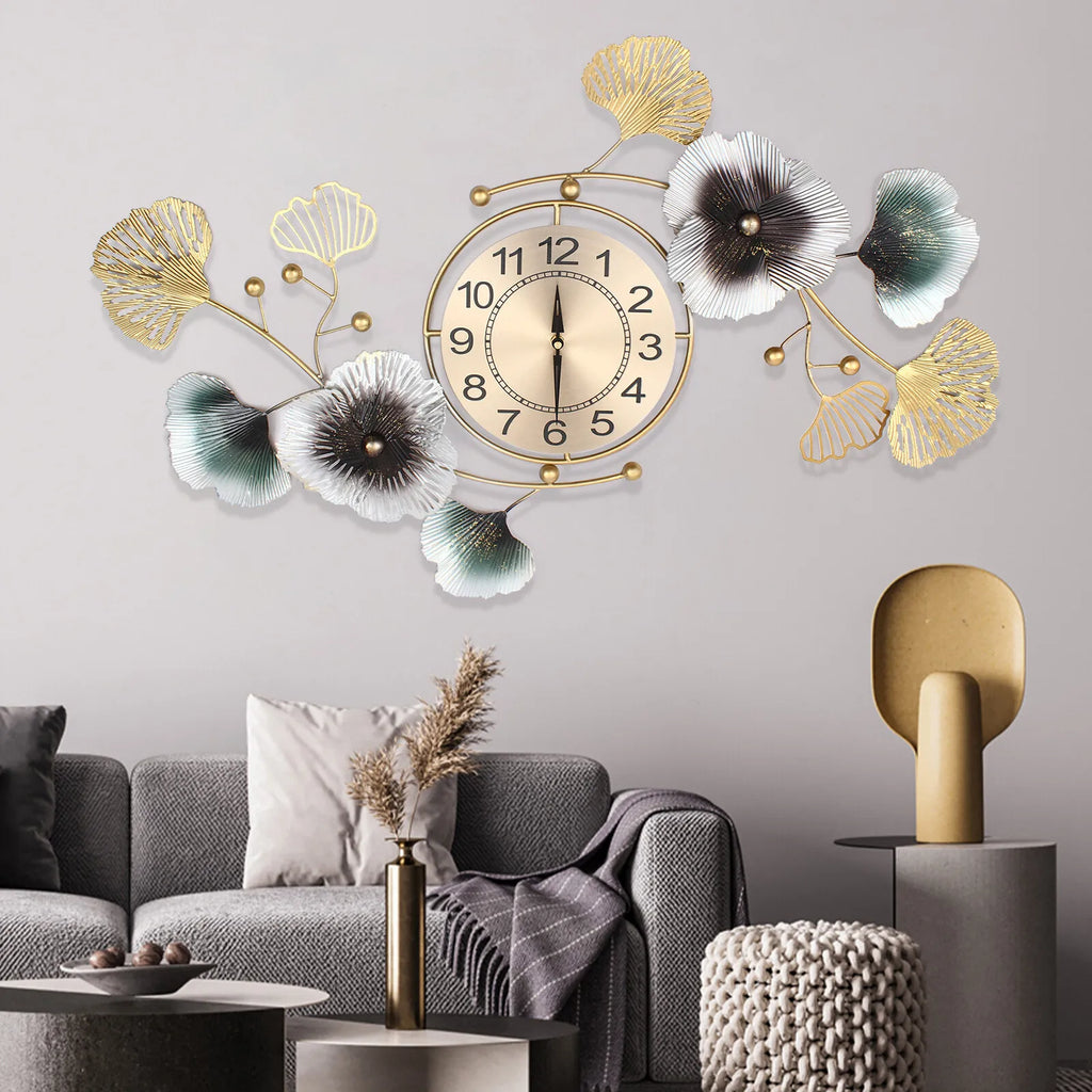 Large wall clock with ginkgo leaf design in gold and silver, mounted on a gray wall in a modern living room setting.