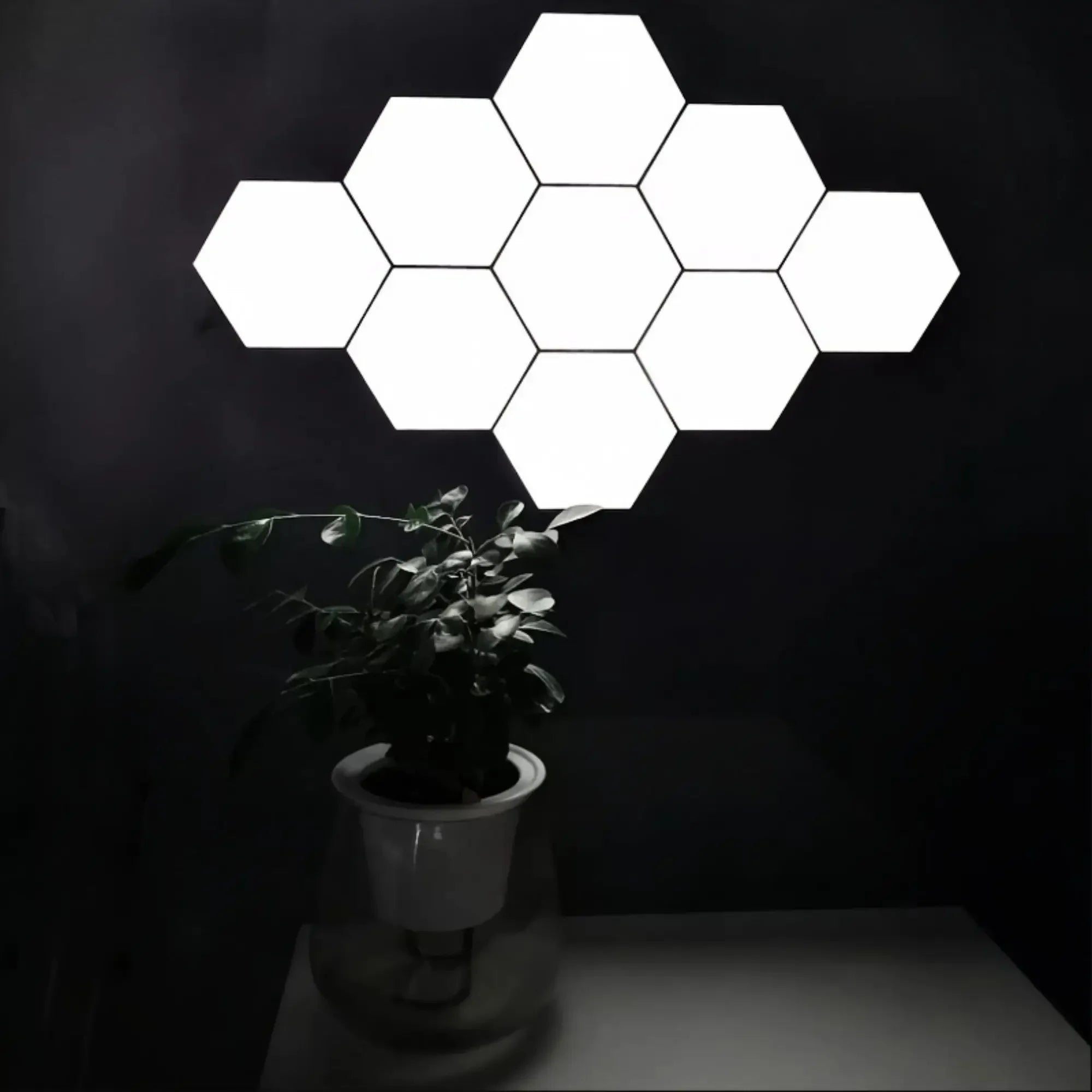 Hexagonal touch LED wall light emitting neutral white light in a 6-pack configuration, mounted on a dark wall above a potted plant.