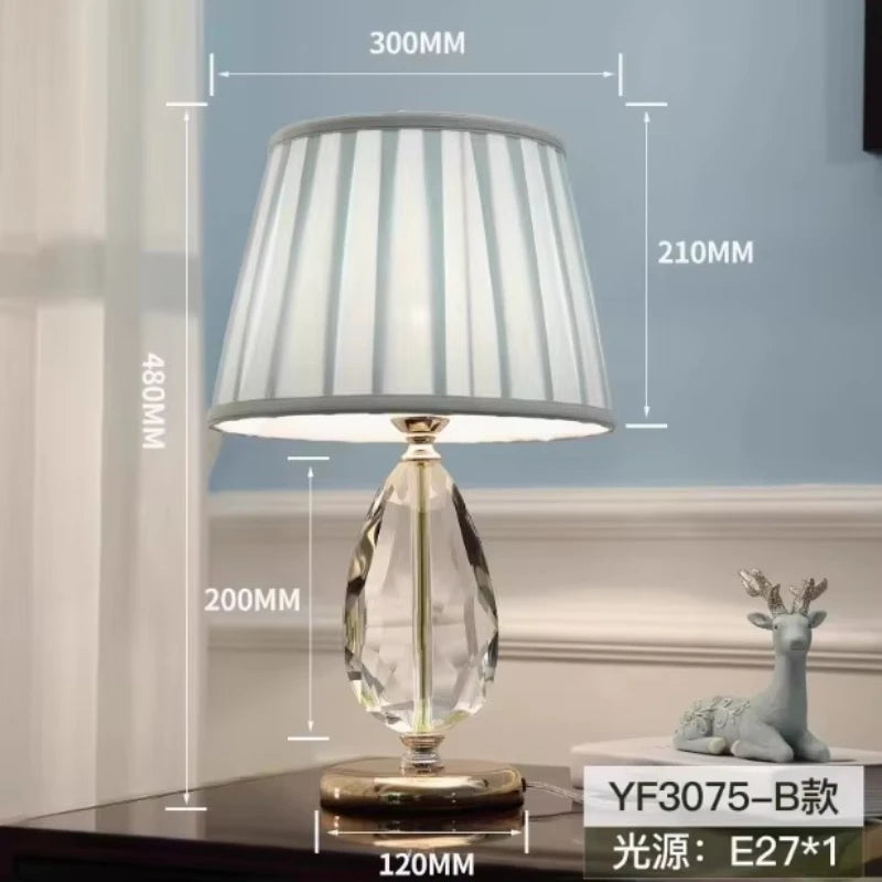 Elegant table lamp with crystal base and pleated shade, displaying dimensions on a wooden surface with a decorative deer figurine.