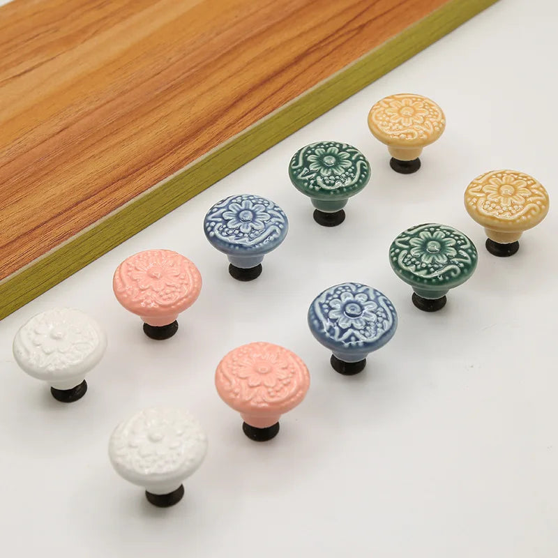 Assorted vintage ceramic drawer knobs with floral designs in white, pink, blue, green, and yellow on a white surface.