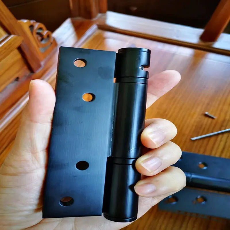 Black stainless steel door hinge with screw holes held in hand, suitable for furniture and cabinet fittings.